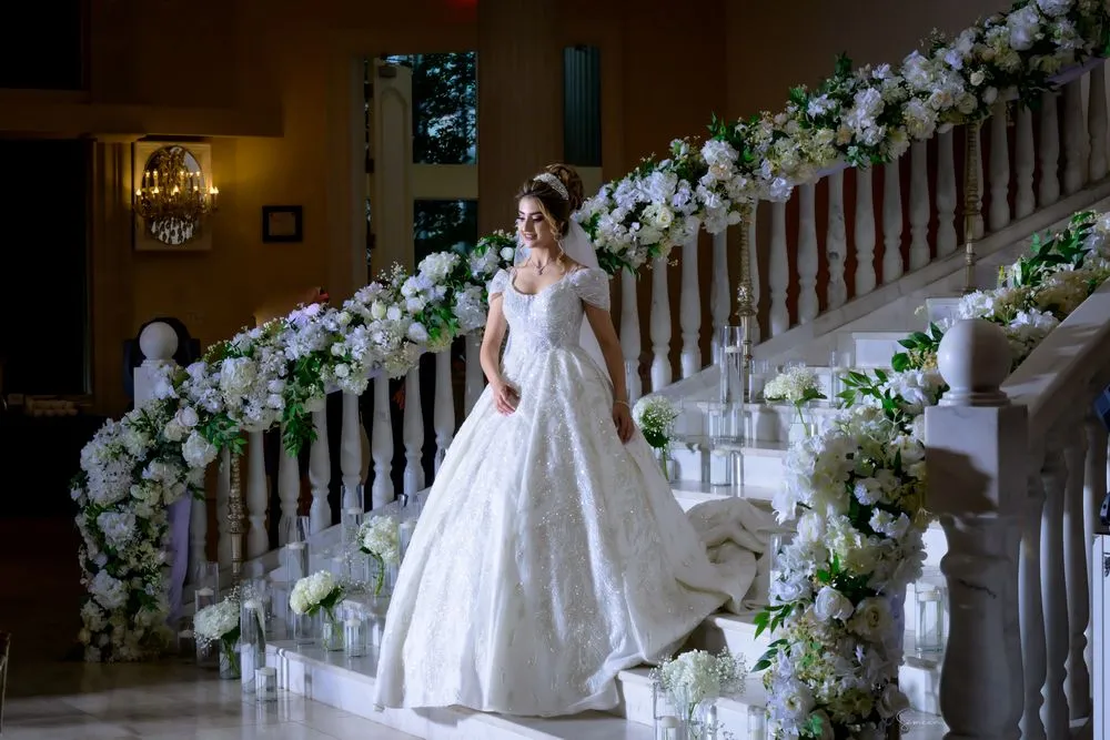 Bride in a white gown on a flower-lined staircase